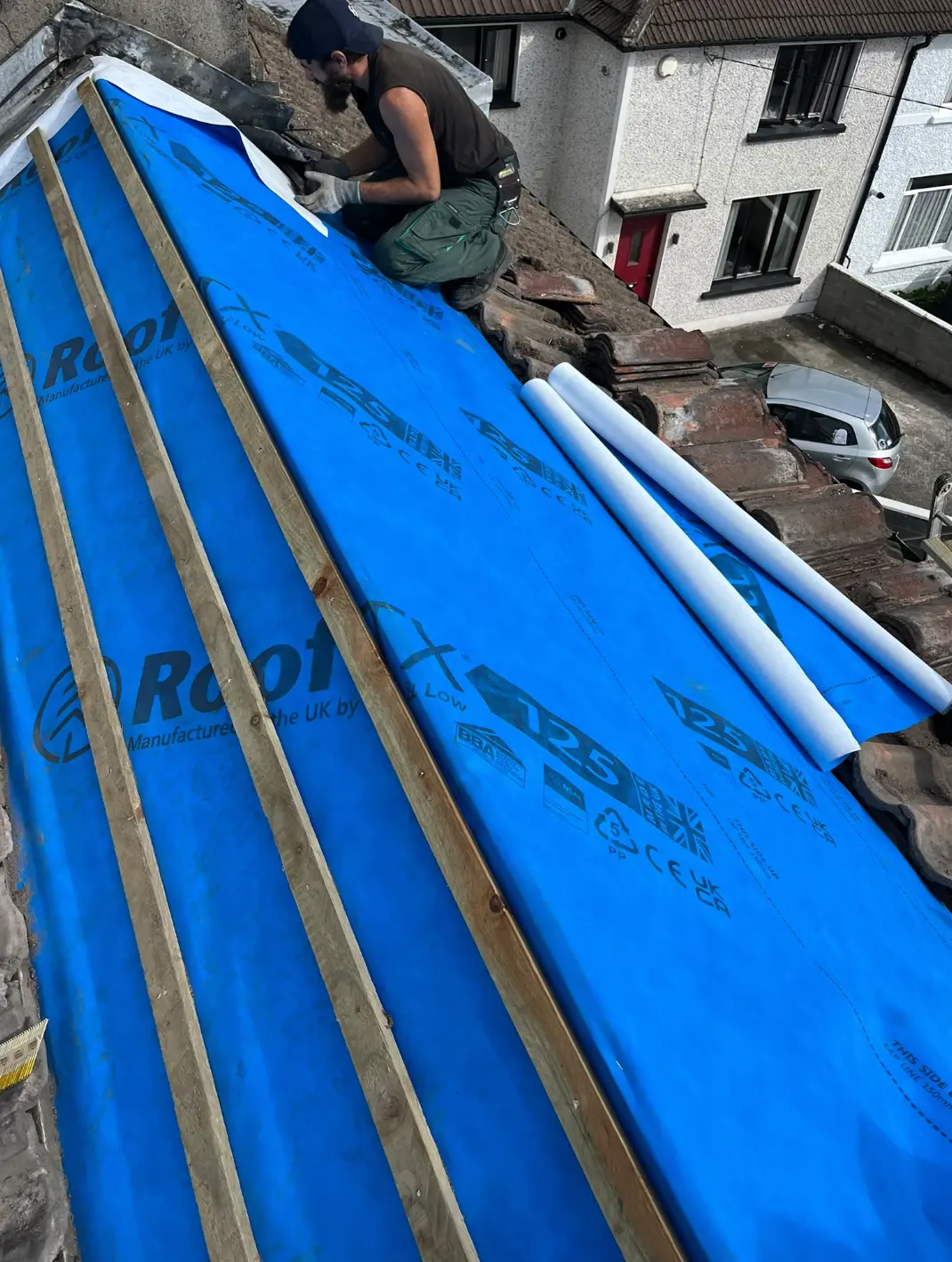 Roofer fitting blue waterproof membrane to a pitched roof